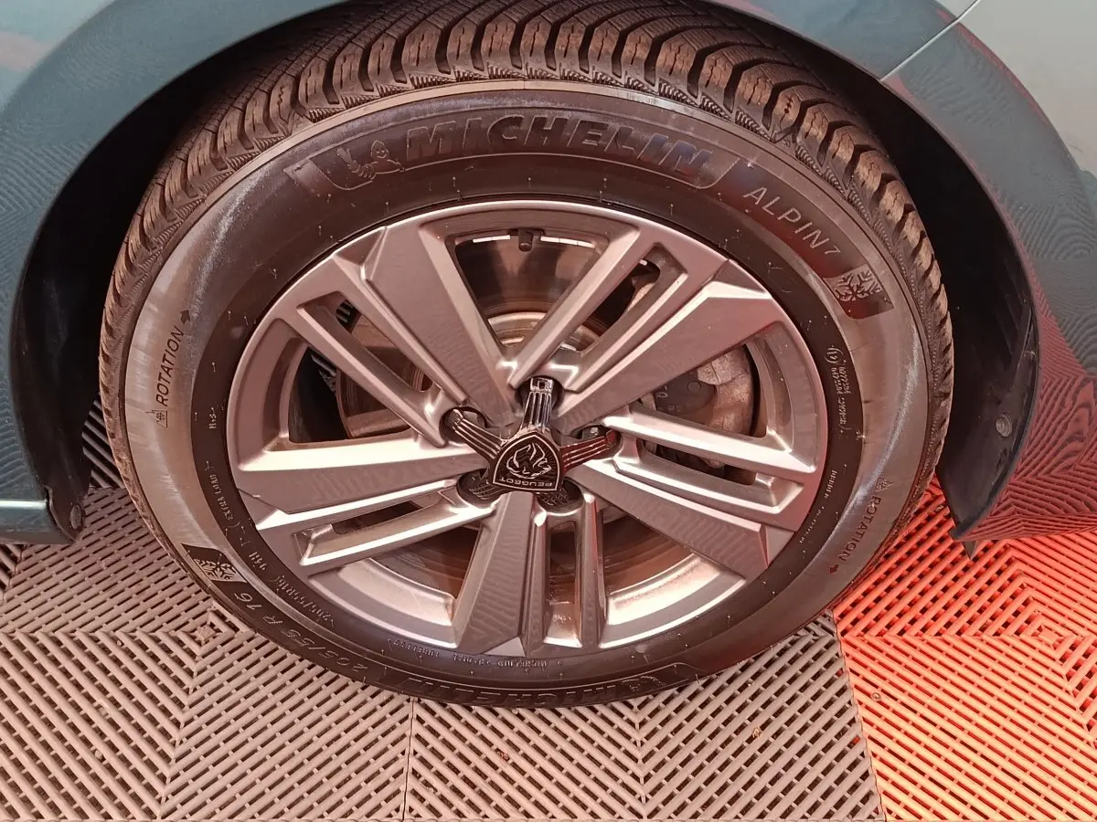 Gros plan sur la roue avant droite d'une Peugeot 308 2023, jante alliage grise et pneu Michelin Alpin 7.