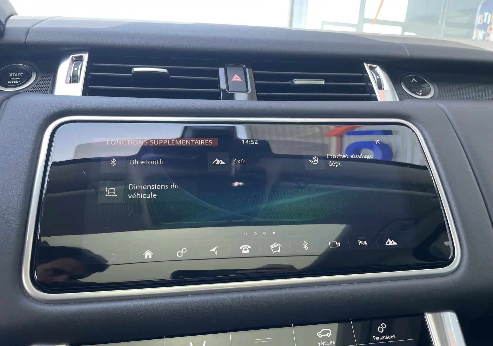 Écran tactile central du Range Rover Sport gris, affichant les fonctions Bluetooth et crochet d'attelage, vue intérieure frontale.