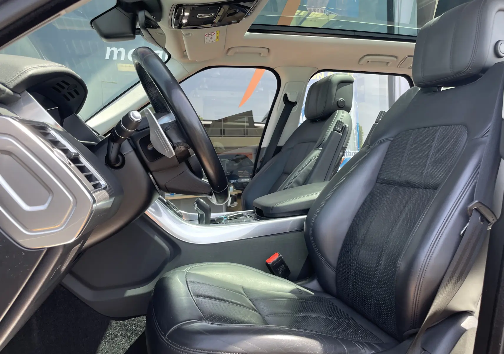 Vue intérieure côté conducteur du Range Rover Sport 2021 avec sellerie cuir noir et toit panoramique lumineux.