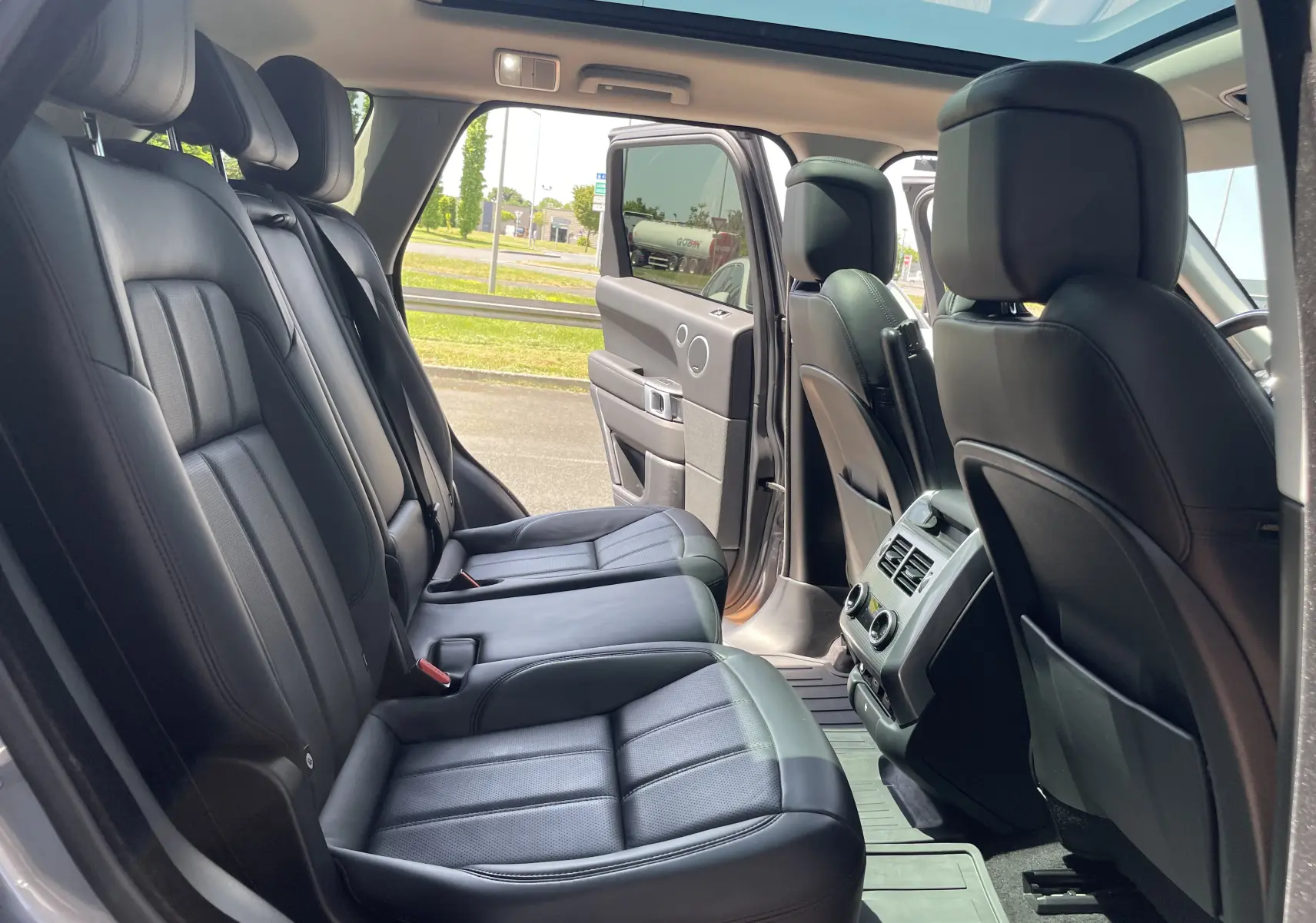 Vue intérieure côté gauche du Range Rover Sport gris Eiger, montrant les sièges arrière en cuir noir et le toit panoramique ouvert.
