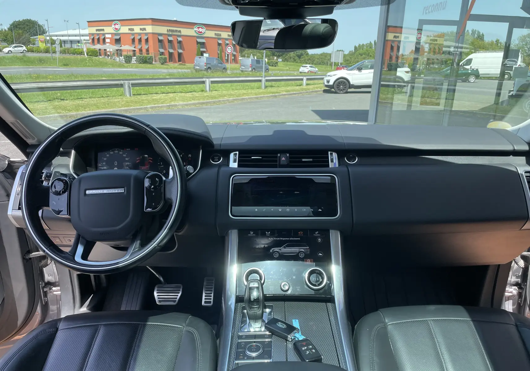 Vue intérieure avant du Range Rover Sport gris Eiger, tableau de bord moderne avec écran tactile et volant cuir multifonction.
