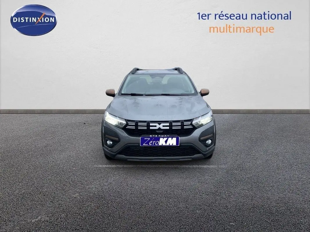 Vue frontale d'une Dacia Sandero Stepway gris schiste métal avec calandre noire et feux allumés sur fond neutre.