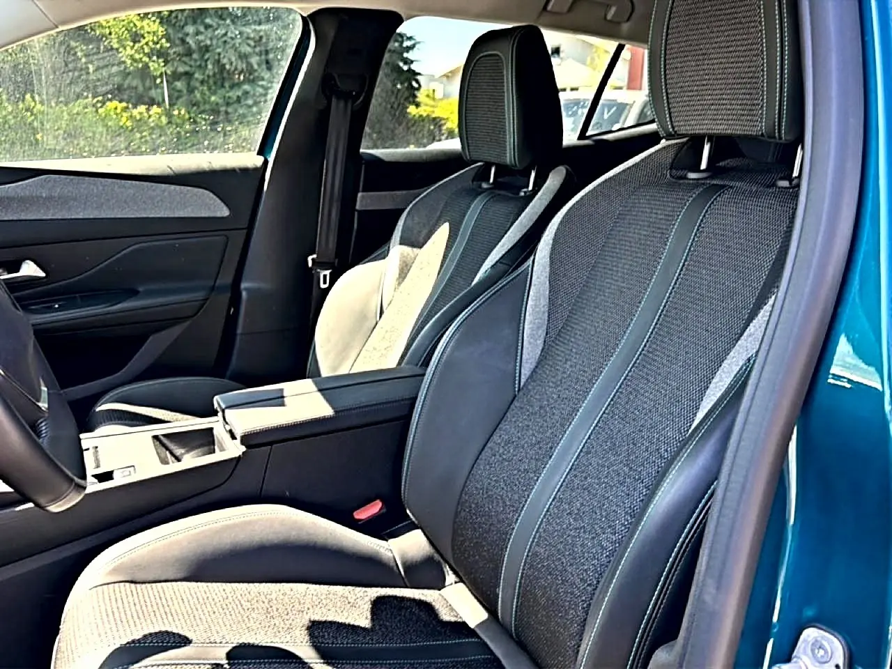 Vue intérieure côté conducteur du Peugeot 408 Hybrid 145 allure e-dcs6 bleu, sièges tri-matières et accoudoir central visible.