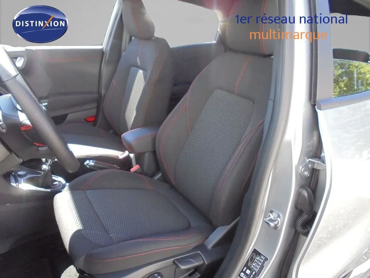 Vue intérieure côté conducteur du Ford Puma gris Solar Metal, sièges tissu noir avec surpiqûres rouges et boîte manuelle visible.