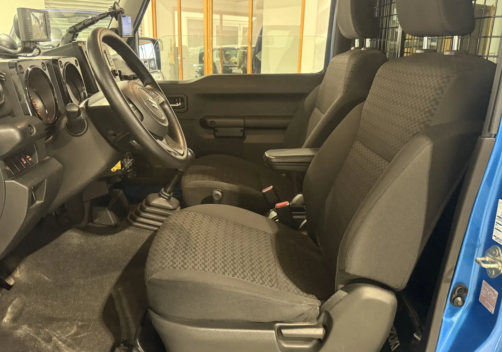 Intérieur du Suzuki Jimny 2021 bleu, vue côté conducteur montrant les sièges noirs et la boîte manuelle.