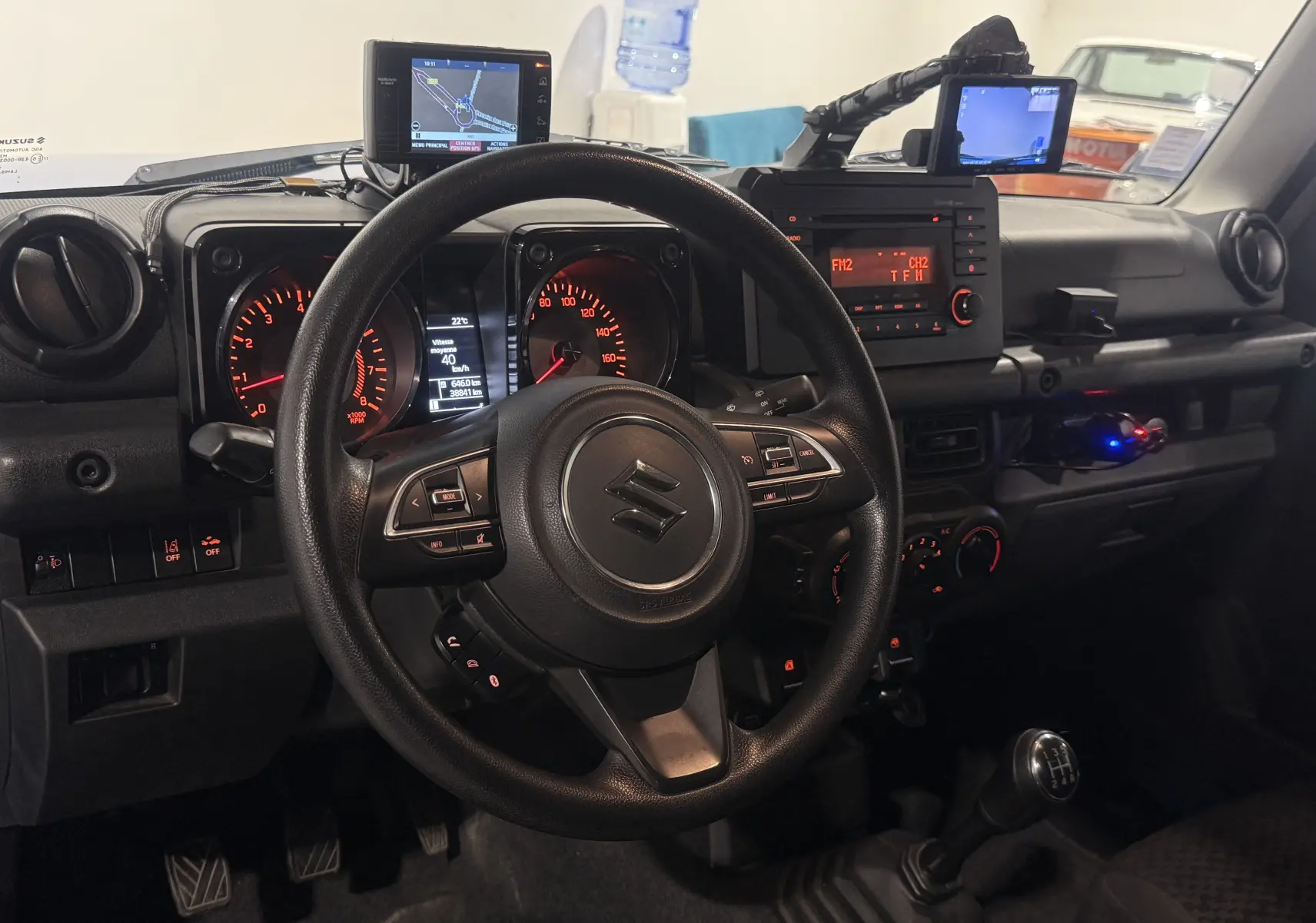 Vue intérieure du tableau de bord du Suzuki Jimny bleu 2021, volant multifonction et levier de vitesses manuel visibles.