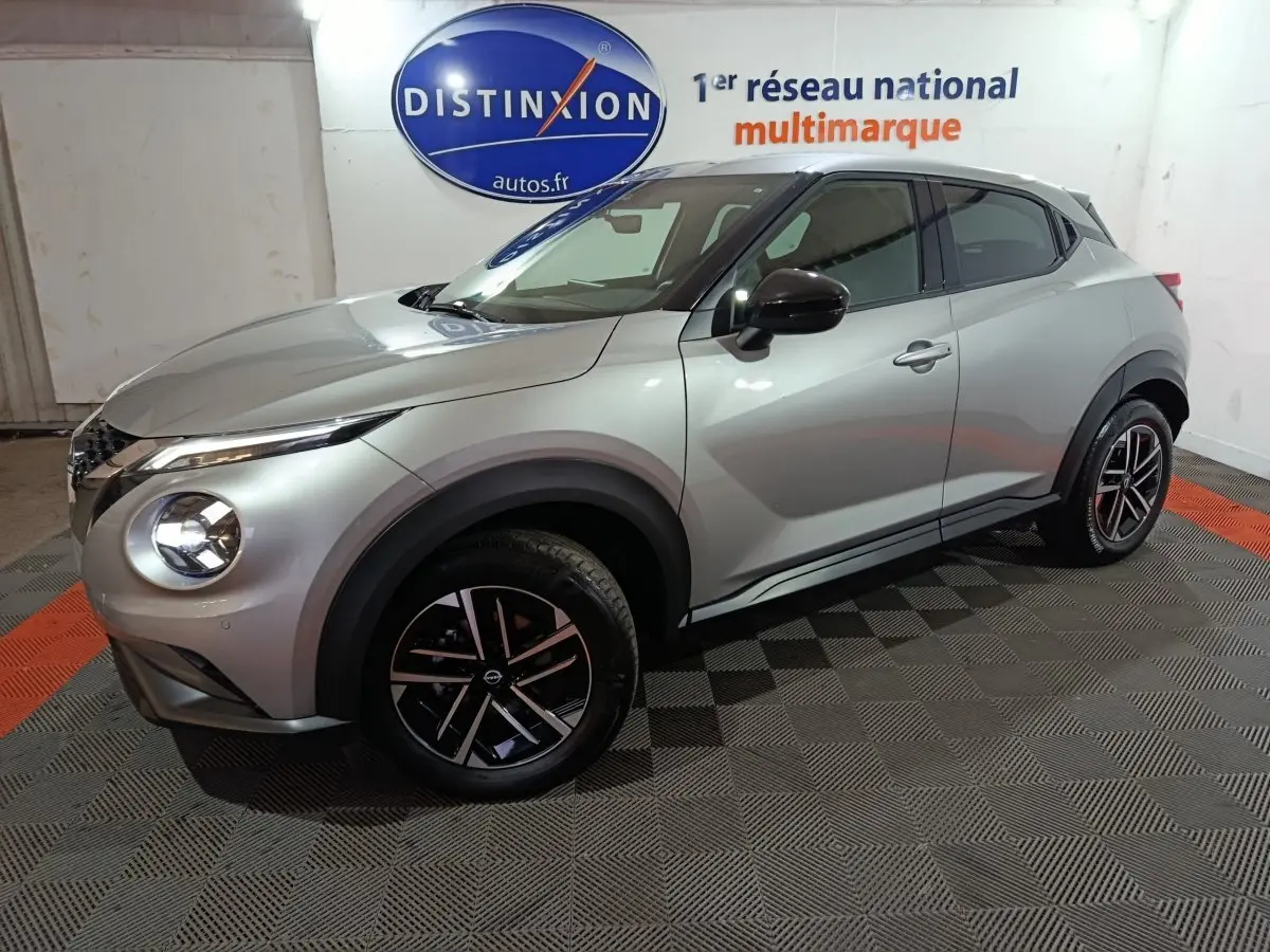 Vue 3/4 avant droite du Nissan Juke gris foncé 2025 avec jantes noires et phares LED allumés.