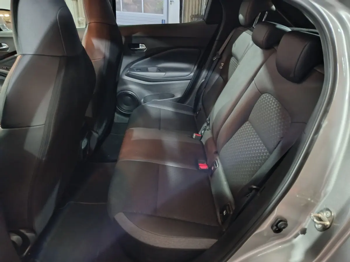 Vue côté droit de l'intérieur arrière du Nissan Juke gris foncé, montrant la banquette en tissu noir et les portières.