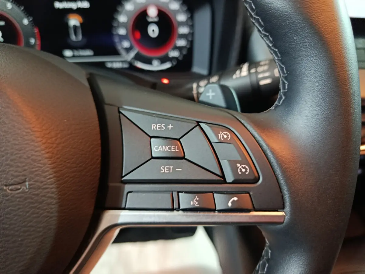 Gros plan sur les commandes de régulateur de vitesse et téléphone au volant noir du Nissan Juke gris foncé 2025.