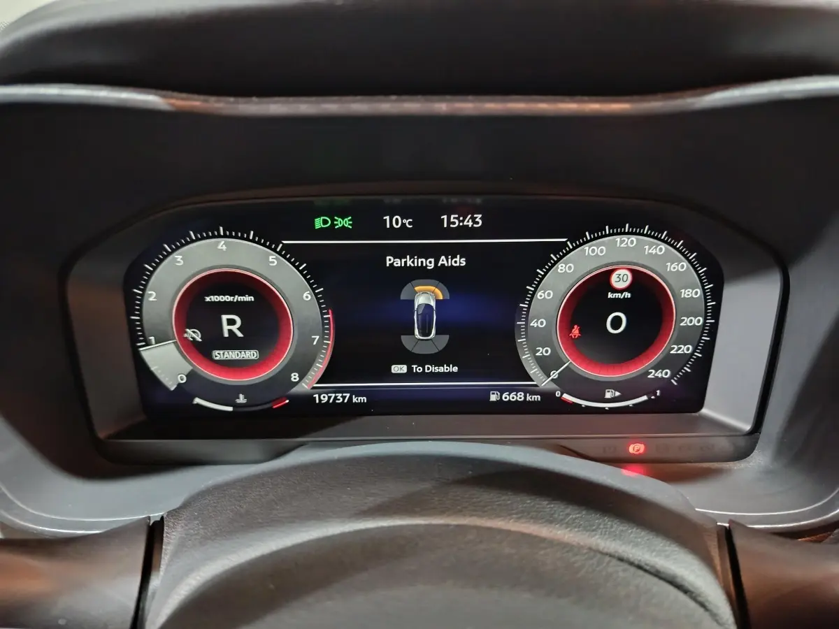 Vue rapprochée du combiné d'instruments numérique du Nissan Juke gris foncé, affichant l'aide au stationnement et la vitesse à 0 km/h.