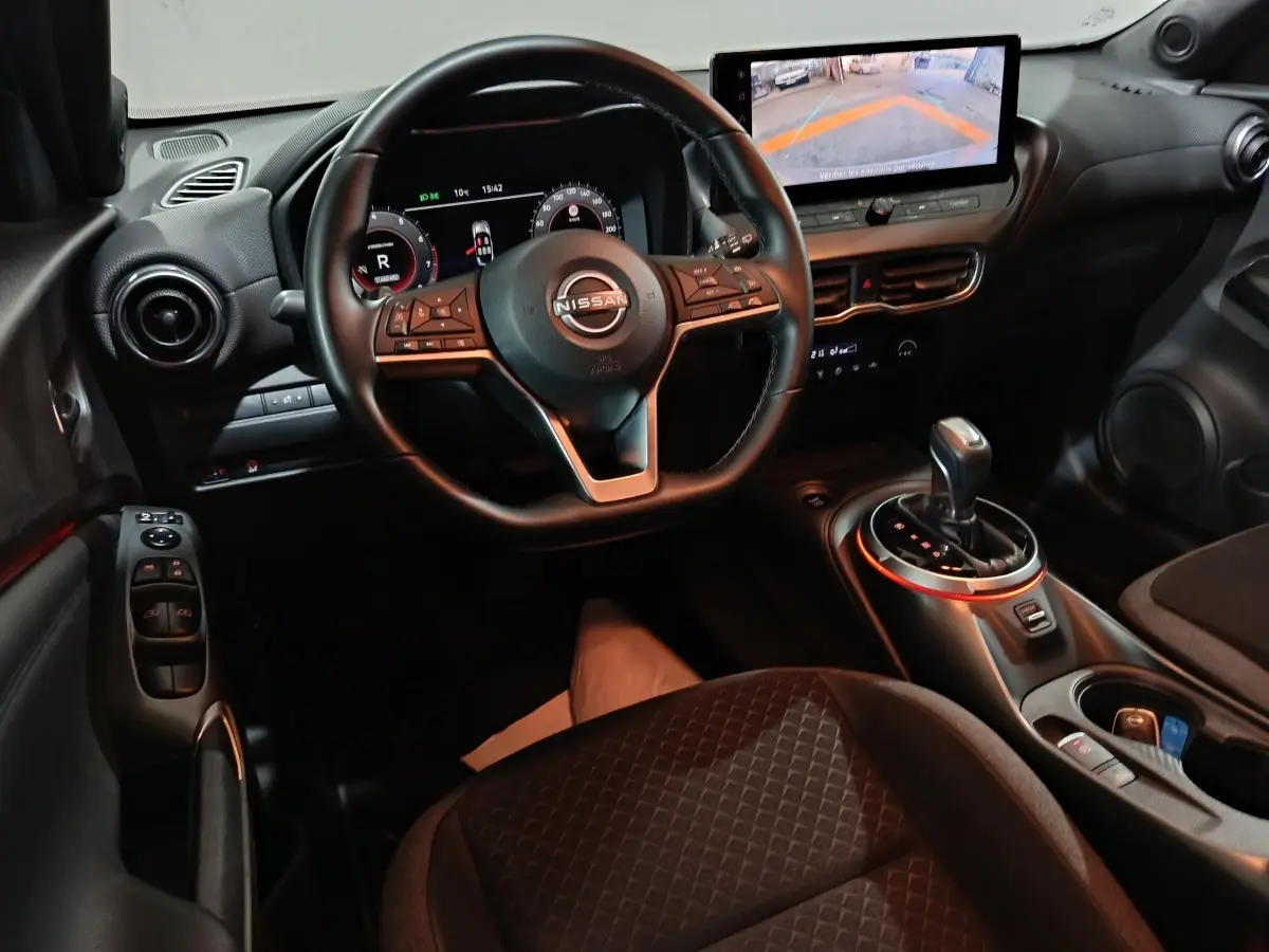 Intérieur du Nissan Juke gris foncé, vue du poste de conduite avec volant multifonction et écran tactile central affichant la caméra de recul.