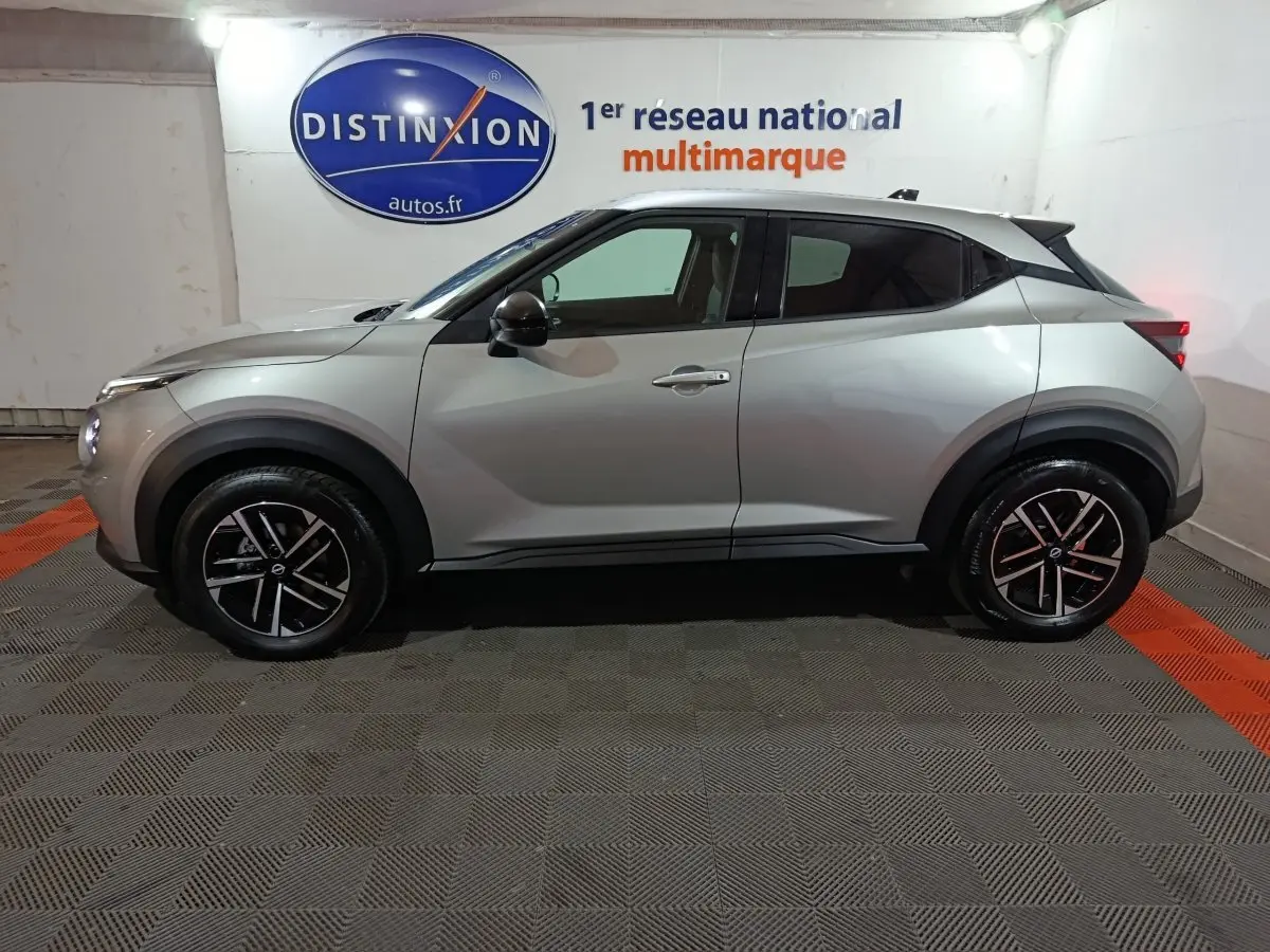 Vue de profil côté gauche d'un Nissan Juke gris foncé avec jantes noires et toit blanc dans un showroom.