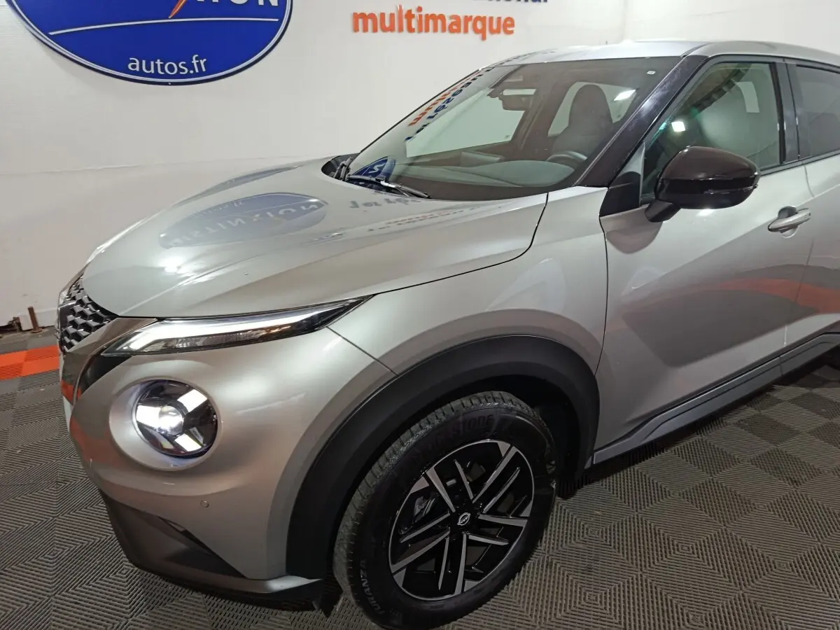 Vue 3/4 avant droit du Nissan Juke 2025 gris foncé avec phares LED allumés et jantes noires distinctives.