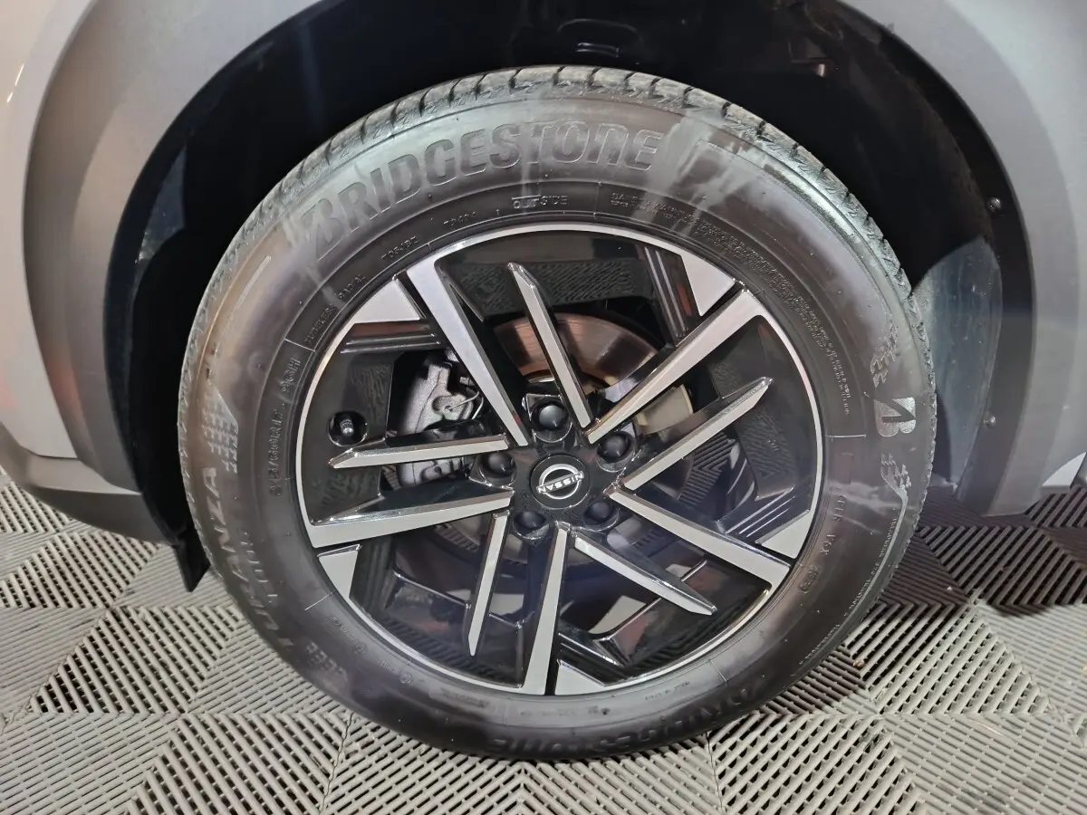 Gros plan sur la roue avant droite du Nissan Juke gris foncé, jante alliage noire à design moderne.