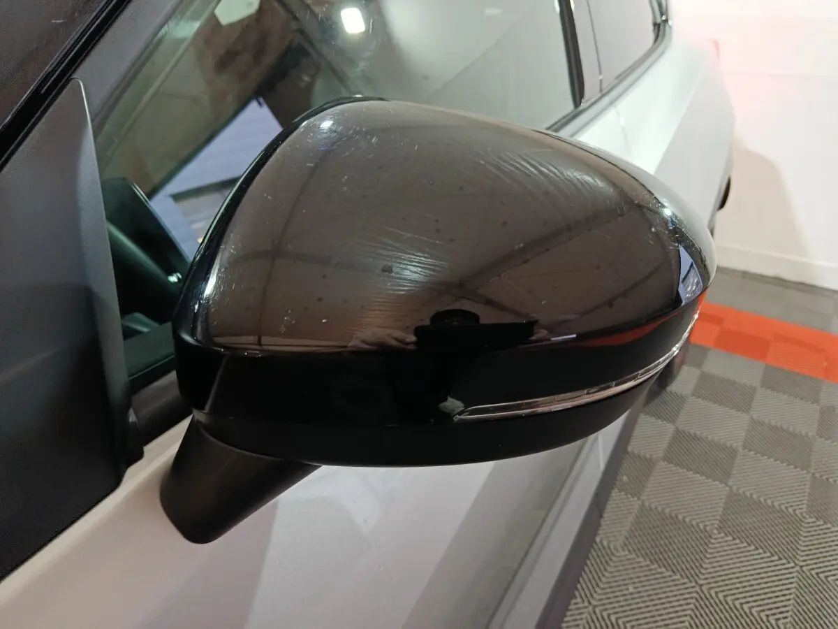 Gros plan sur le rétroviseur droit noir brillant du Nissan Juke gris foncé, avec clignotant intégré visible.