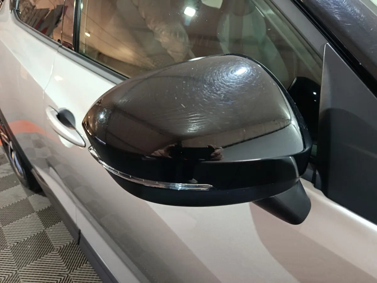 Gros plan sur le rétroviseur droit noir brillant du Nissan Juke gris foncé, avec poignée de porte visible en arrière-plan.