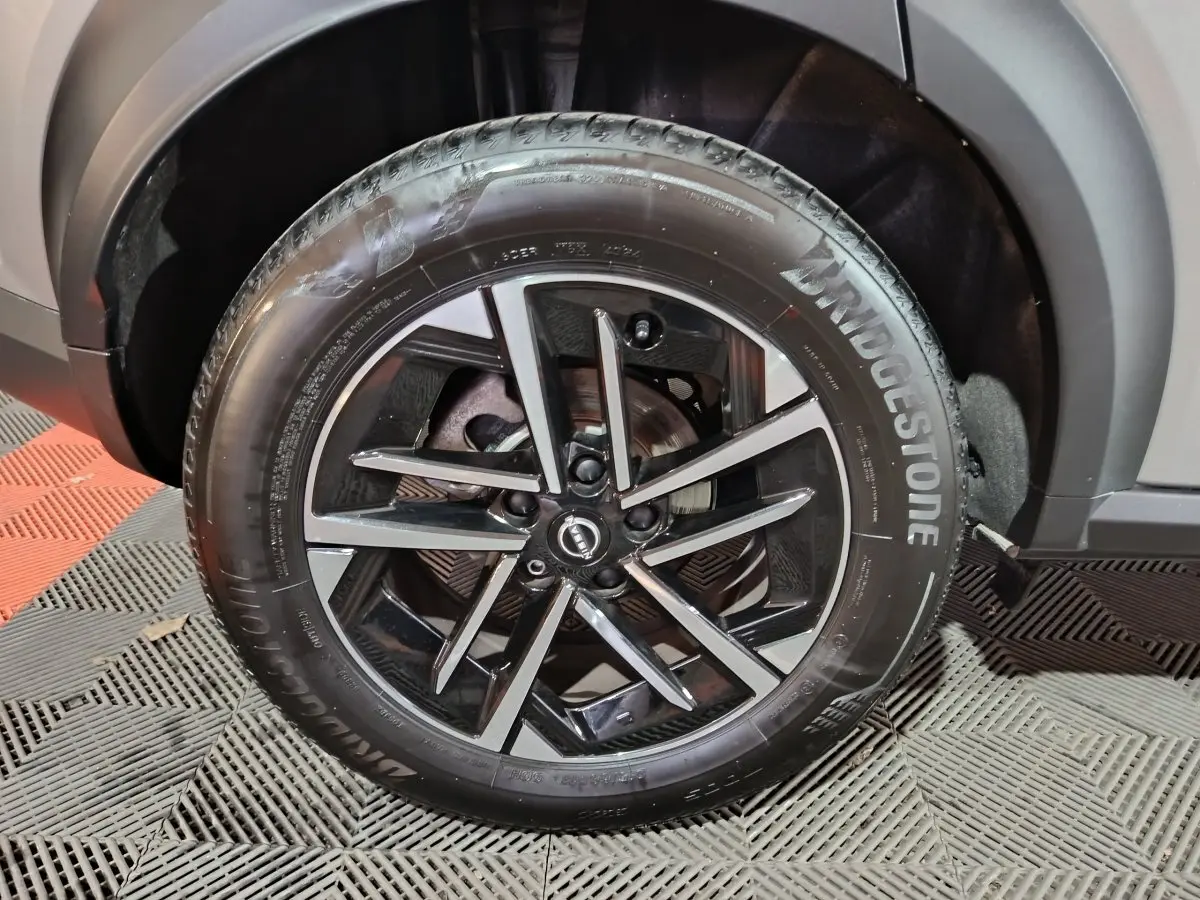 Gros plan sur la roue avant droite du Nissan Juke gris foncé, mettant en valeur la jante noire brillante et le pneu Bridgestone.