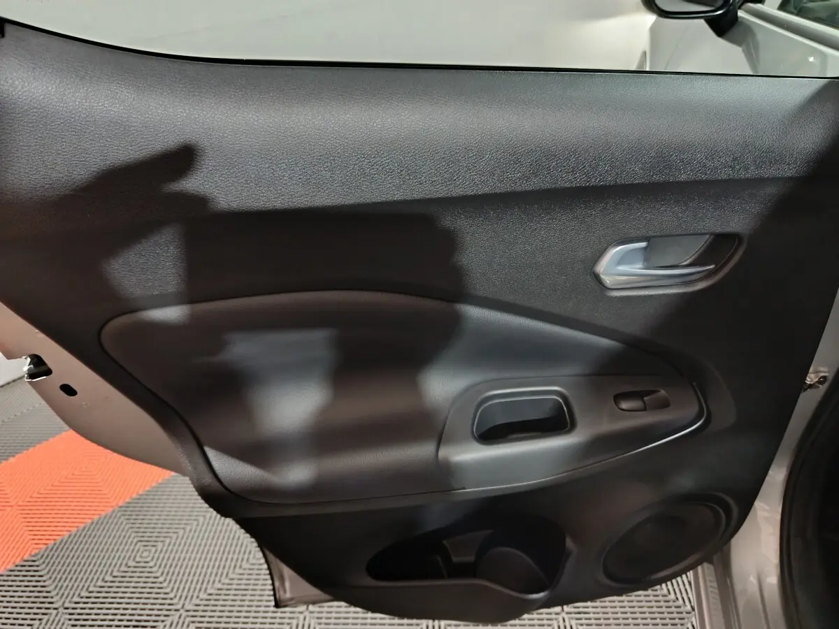 Gros plan sur la porte intérieure côté droit du Nissan Juke gris foncé, montrant la poignée et les commandes de fenêtre.