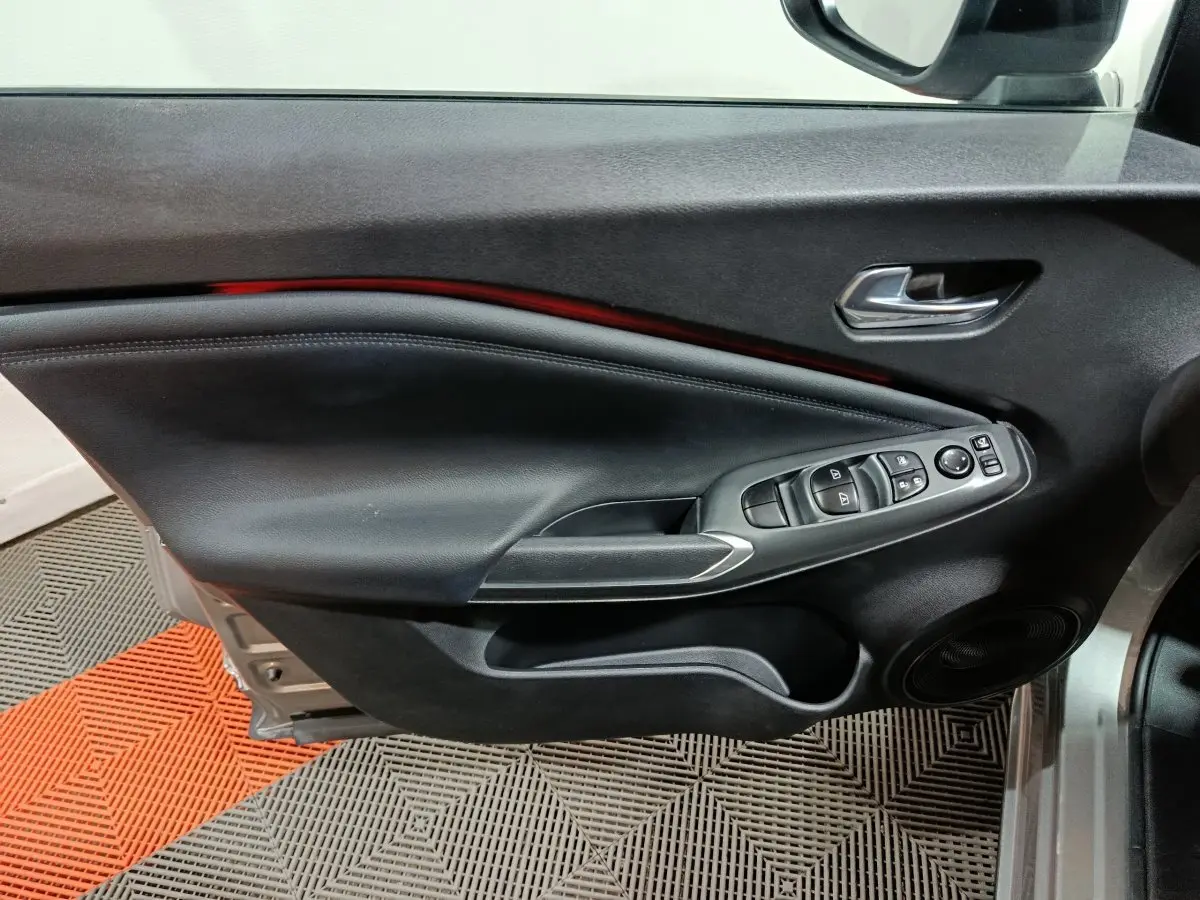 Vue rapprochée de la porte avant gauche intérieure du Nissan Juke gris foncé, avec commandes de vitres et rétroviseur.