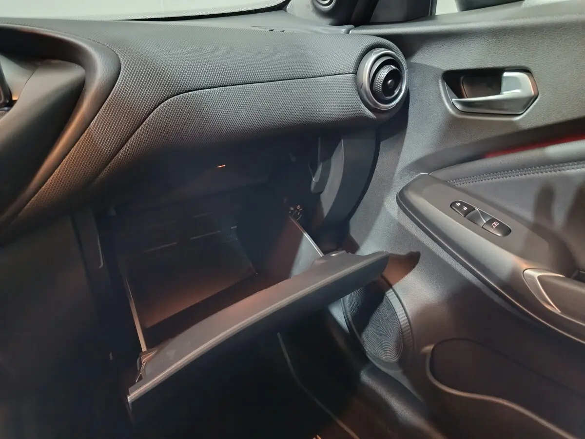 Intérieur noir du Nissan Juke 2025, vue côté passager avec boîte à gants ouverte et détails de la portière.