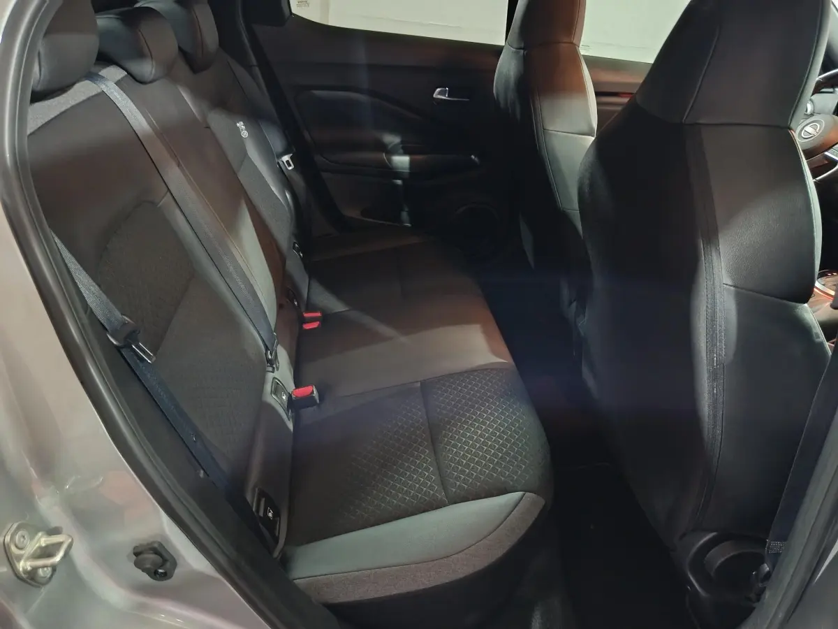 Vue intérieure côté gauche sur la banquette arrière noire du Nissan Juke gris foncé avec sièges tissu et ceintures visibles.