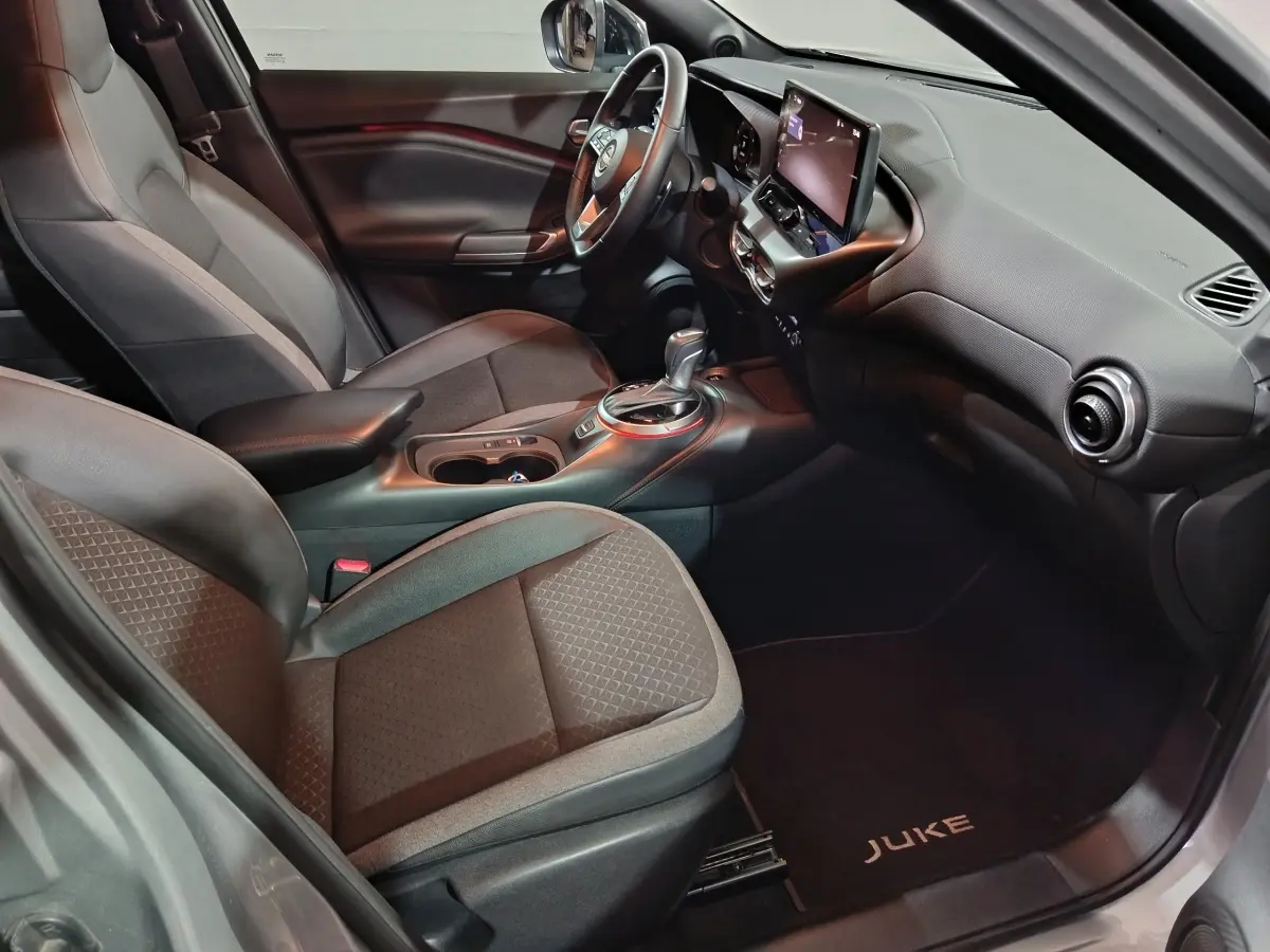 Vue intérieure côté passager du Nissan Juke gris foncé 2025, avec tableau de bord moderne et écran tactile central.