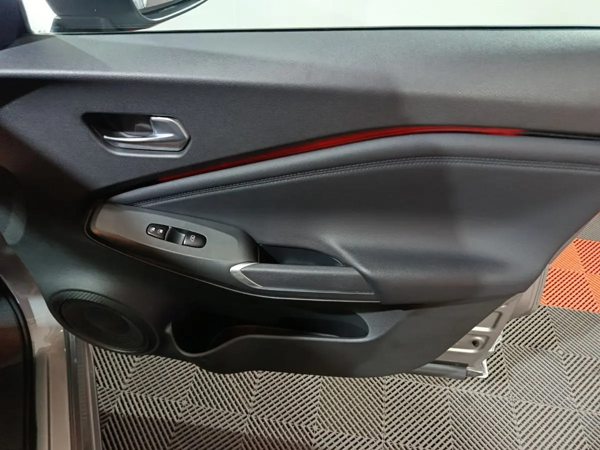 Vue intérieure côté gauche de la porte avant d’un Nissan Juke gris foncé avec éclairage d’ambiance rouge et commandes de vitres.