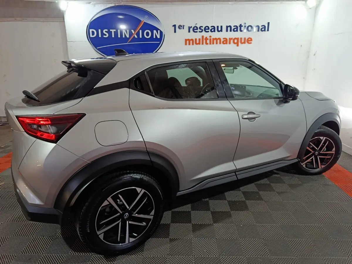 Vue latérale droite du Nissan Juke gris foncé 2025 avec jantes noires et toit noir contrasté dans un showroom.