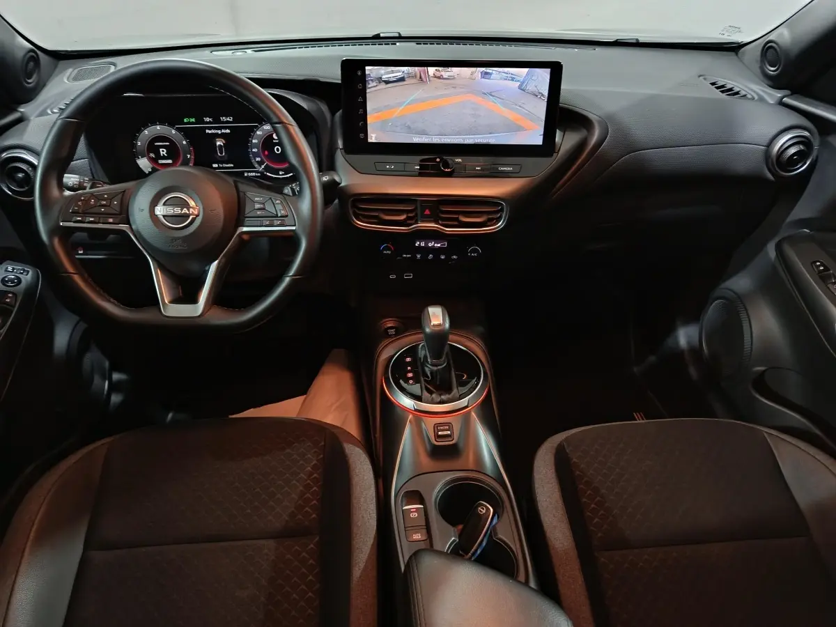 Vue intérieure frontale du Nissan Juke gris foncé 2025, avec tableau de bord numérique et écran tactile central affichant la caméra de recul.