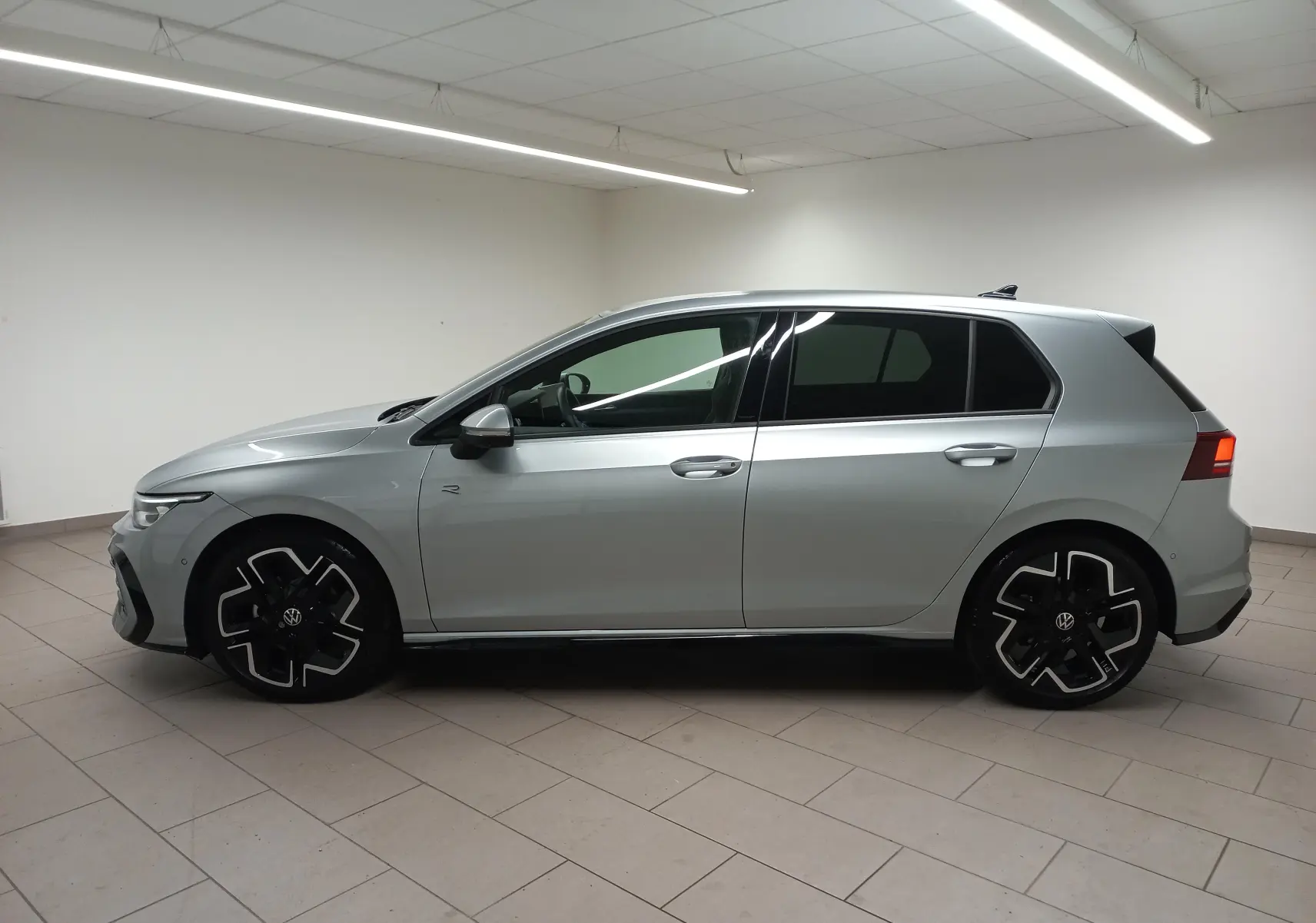 Vue de profil côté gauche d'une Volkswagen Golf 1.5 eTSI R-Line argent dolomite avec jantes noires et vitres teintées.