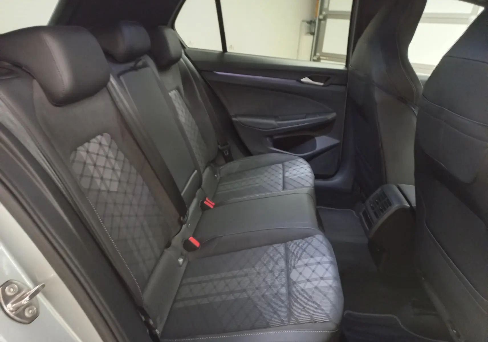 Vue intérieure arrière côté gauche de la Volkswagen Golf 1.5 eTSI R-Line avec sièges en tissu noir à motifs géométriques.