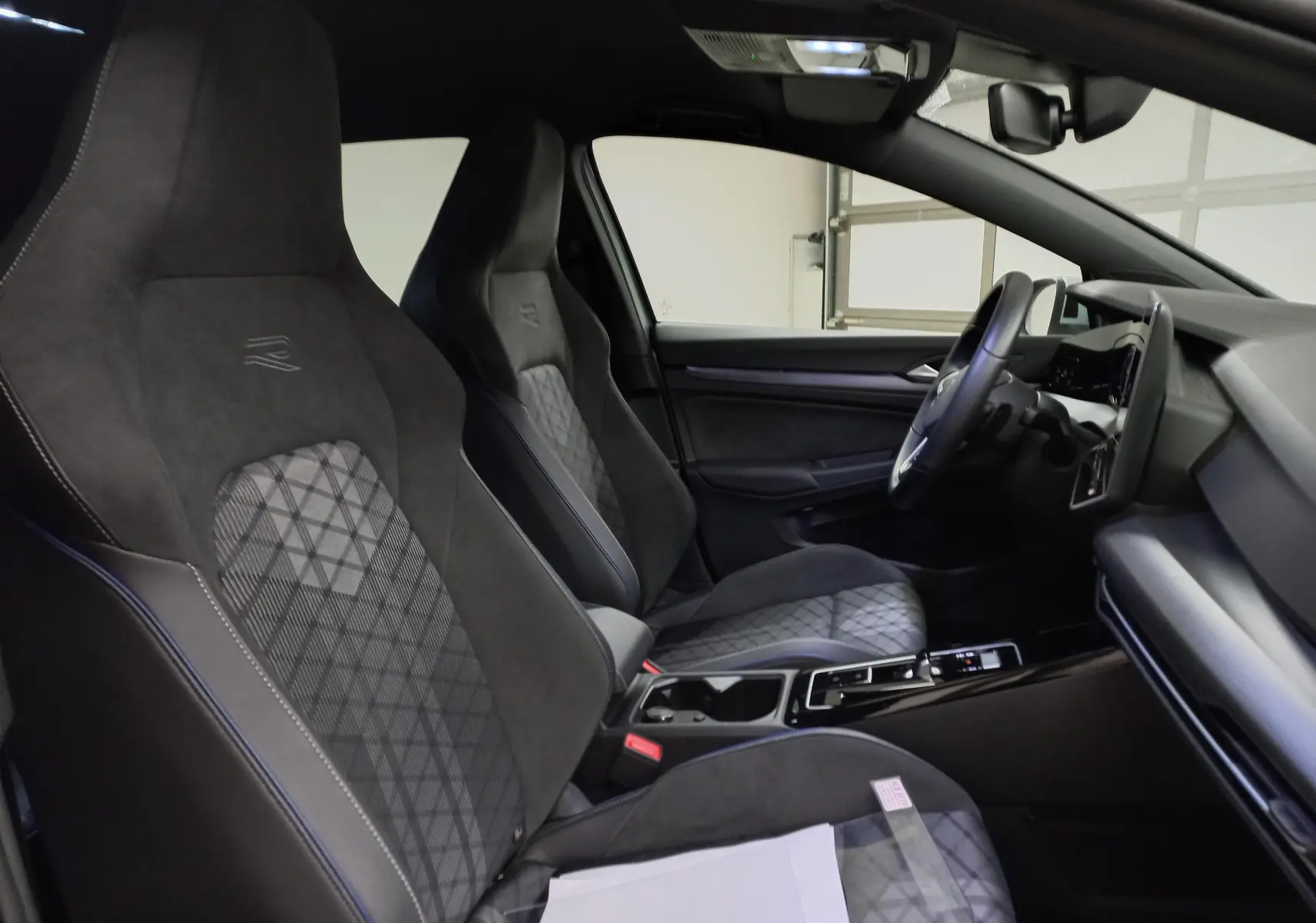 Vue intérieure côté conducteur de la Volkswagen Golf 1.5 eTSI R-Line avec sièges sport en tissu et alcantara noir.