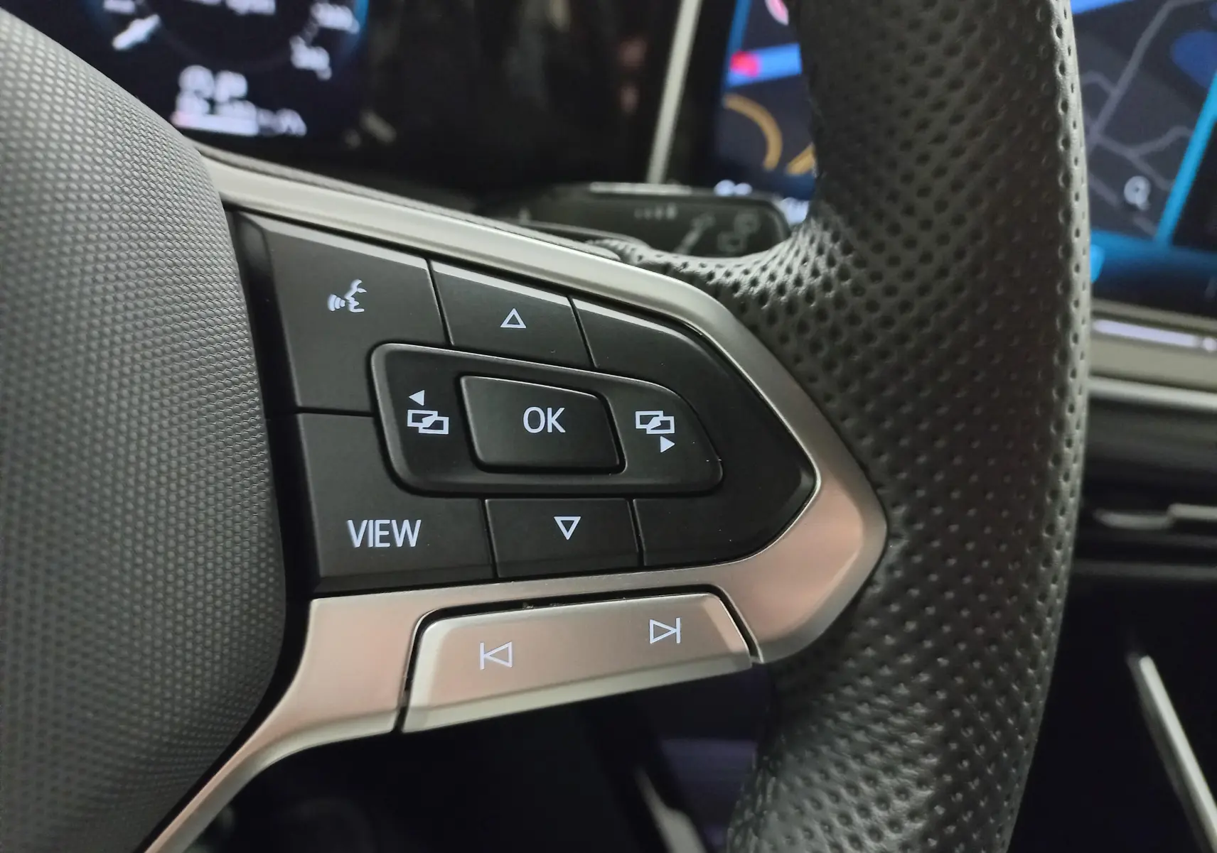 Gros plan sur les commandes au volant en cuir perforé de la Volkswagen Golf 1.5 eTSI R-Line, tableau de bord numérique en arrière-plan.