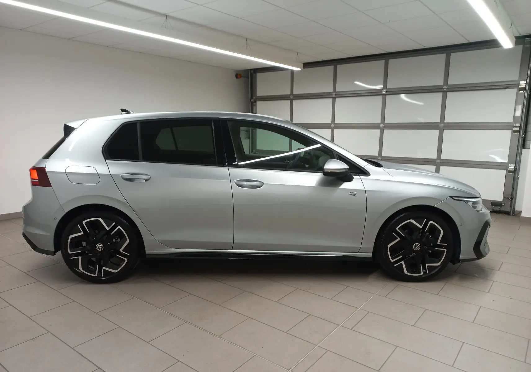 Profil droit d'une Volkswagen Golf 1.5 eTSI R-Line Edition 2025 en argent dolomite, avec jantes noires et détails sportifs.