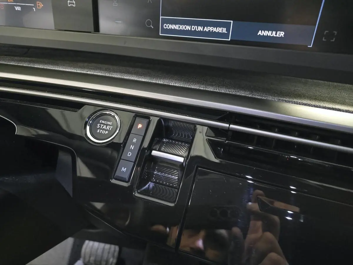 Gros plan sur la console centrale noire laquée du Peugeot 3008 gris 2025, avec bouton start/stop et sélecteur de boîte auto.