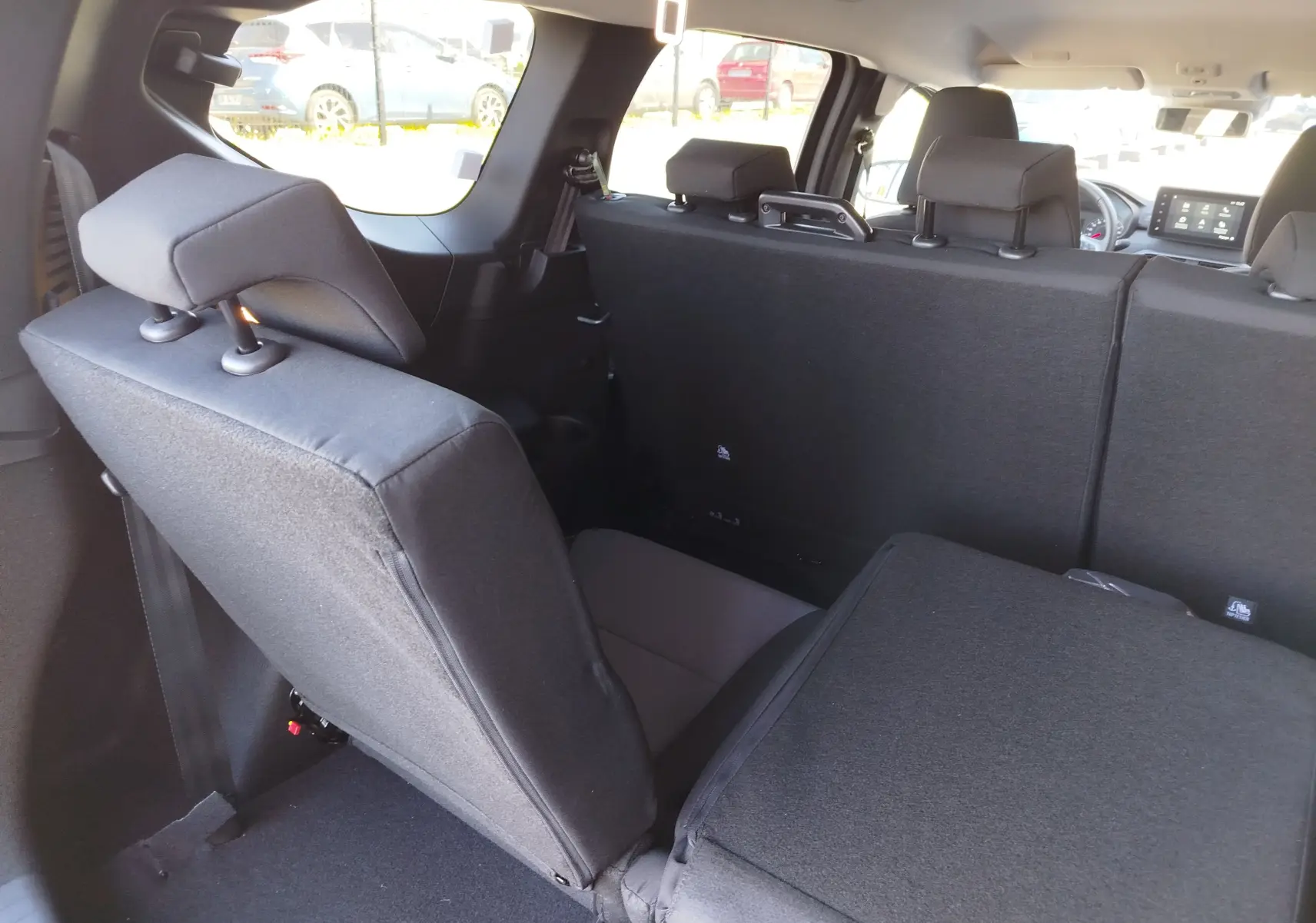 Vue intérieure arrière du Dacia Jogger 2026 montrant les sièges arrière en tissu noir, dont un partiellement rabattu.
