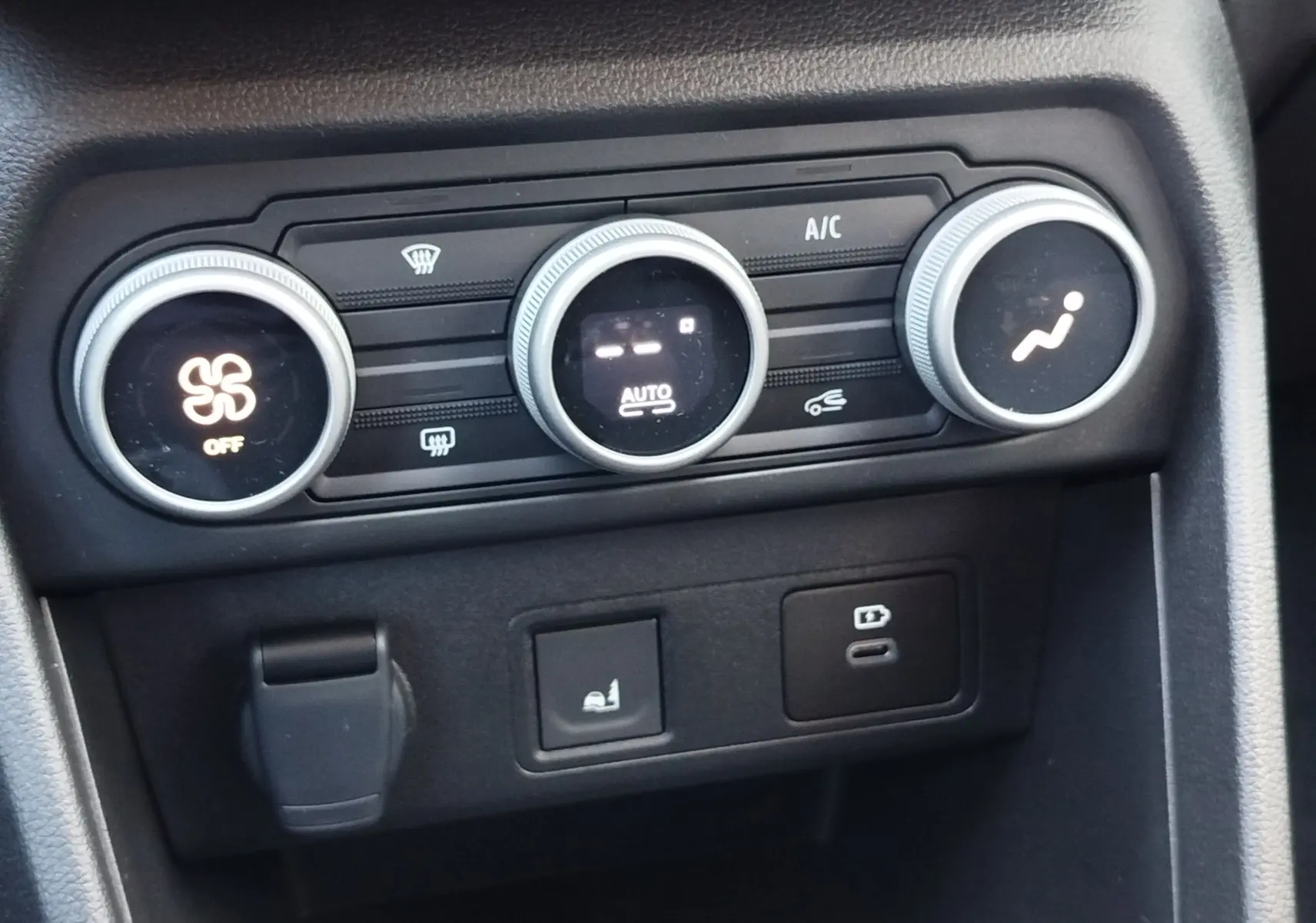 Vue rapprochée des commandes de climatisation et des prises USB dans le tableau de bord noir du Dacia Jogger 2026.