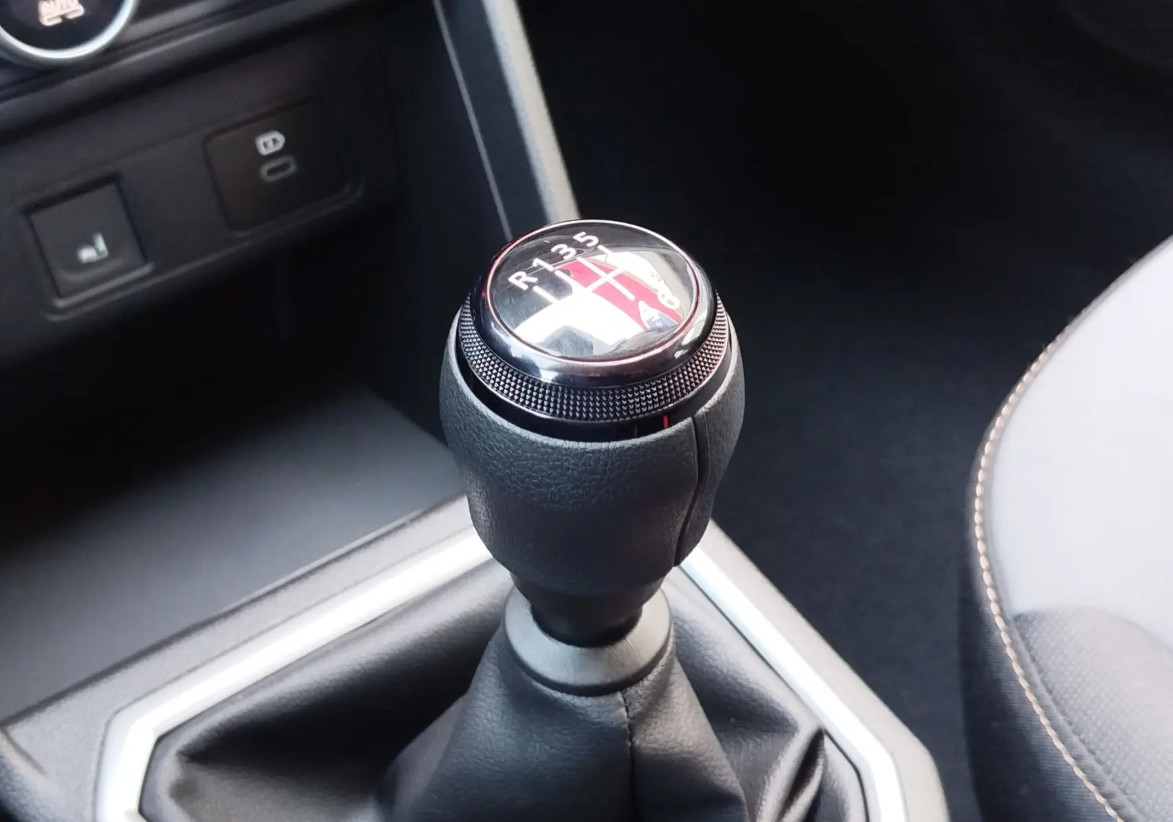 Gros plan sur le levier de vitesses manuel noir du Dacia Jogger, avec coutures apparentes et console sombre en arrière-plan.