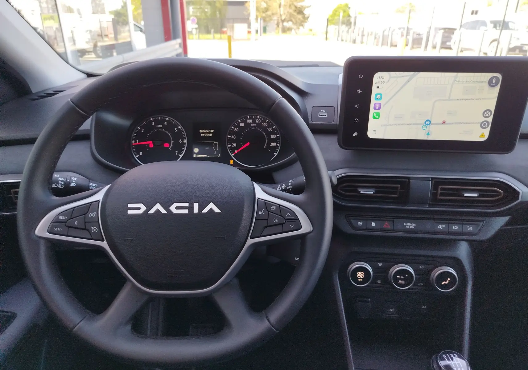 Vue intérieure centrée sur le volant noir DACIA et le tableau de bord avec écran tactile affichant une carte.