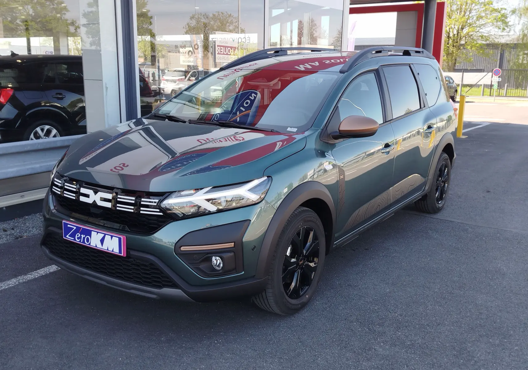 Dacia Jogger 2026 vert cèdre métal en 3/4 avant droit, avec jantes noires et rétroviseurs bronze.