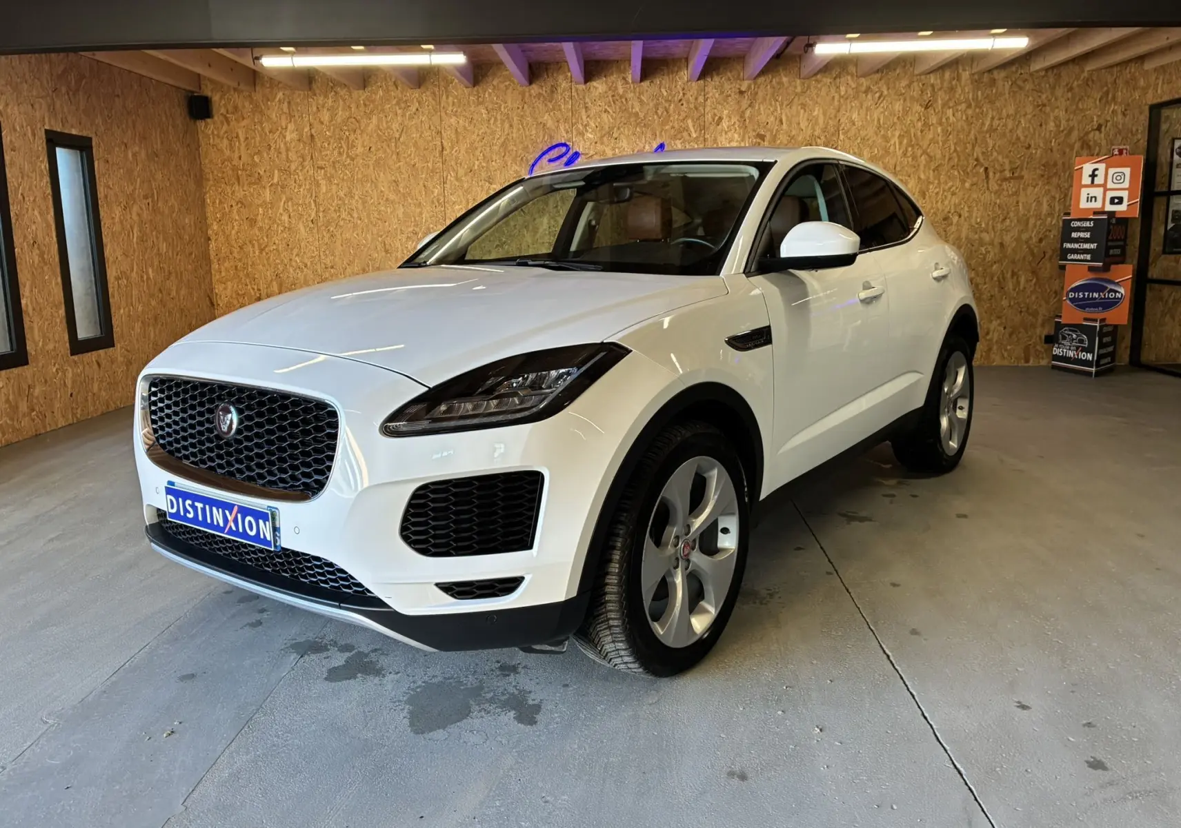 Jaguar E-PACE blanc en 3/4 avant droit dans un garage, avec calandre noire et jantes argentées.