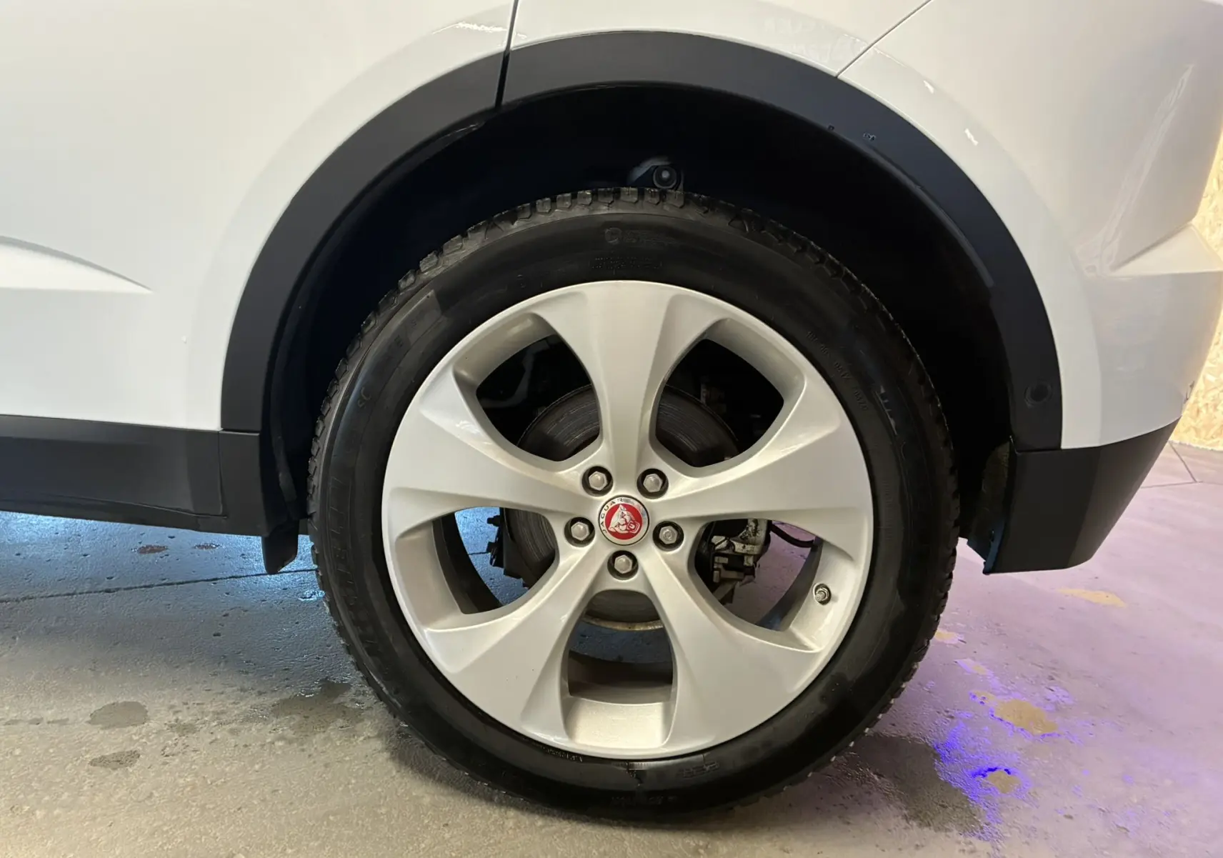 Gros plan sur la roue arrière droite blanche d’un Jaguar E-PACE 2.0D 180 R-DYNAMIC HSE avec jante argentée et logo Jaguar central.