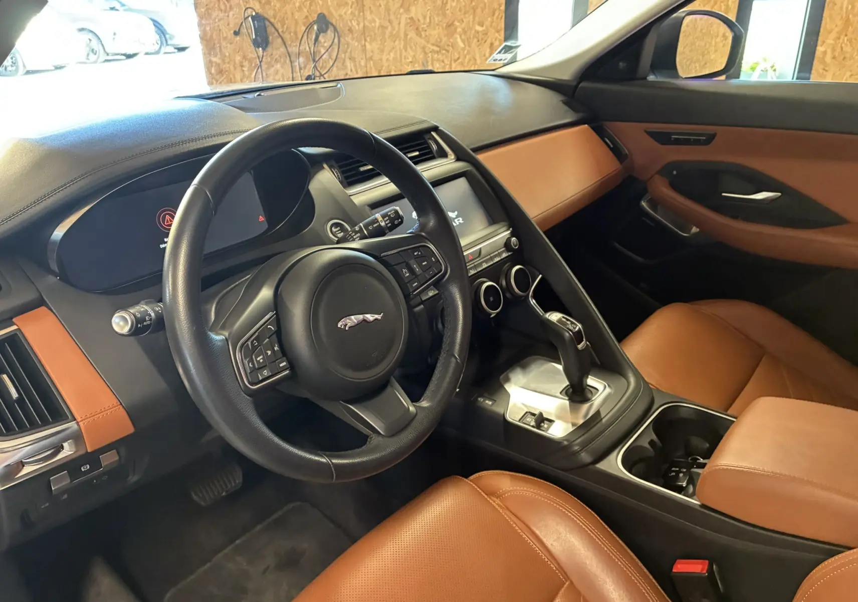 Vue intérieure côté conducteur du Jaguar E-PACE 2019, mettant en valeur le volant noir et les sièges en cuir brun.