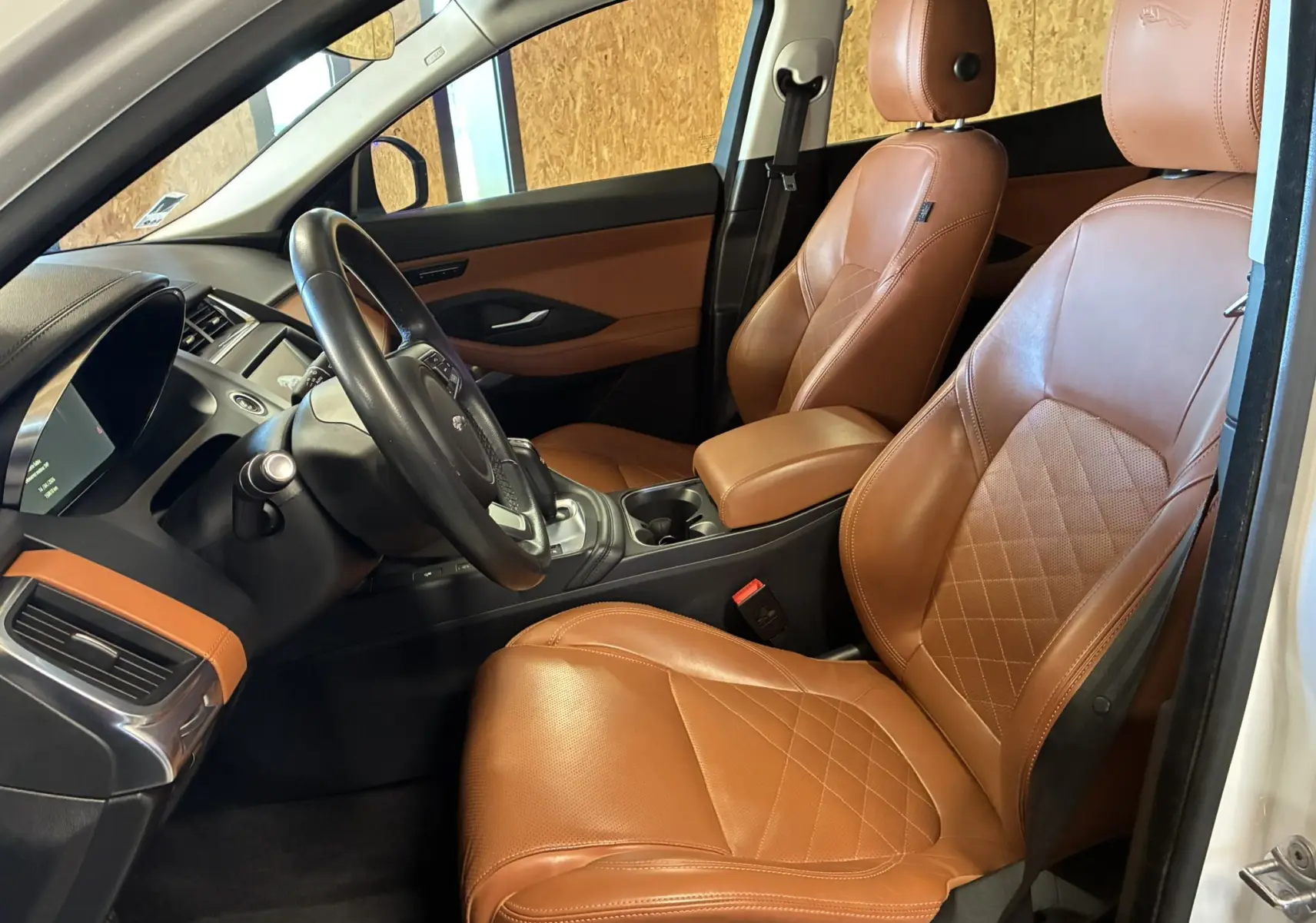 Vue intérieure côté conducteur du Jaguar E-PACE blanc, mettant en valeur les sièges en cuir brun et le tableau de bord moderne.