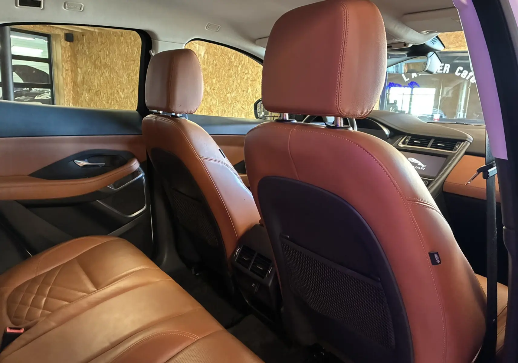 Vue intérieure arrière droite du Jaguar E-PACE blanc 2019, sièges en cuir brun avec finitions élégantes et tableau de bord partiellement visible.