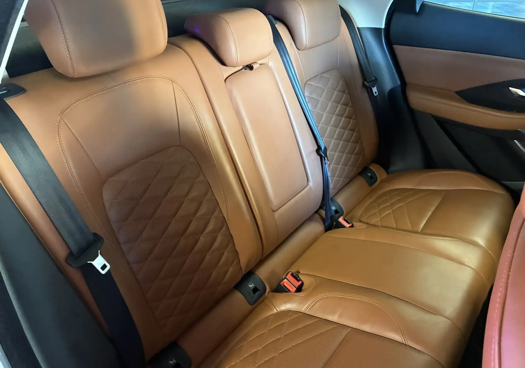 Vue intérieure des sièges arrière en cuir brun matelassé du Jaguar E-PACE 2.0D 180 R-DYNAMIC HSE, avec ceinture de sécurité noire.