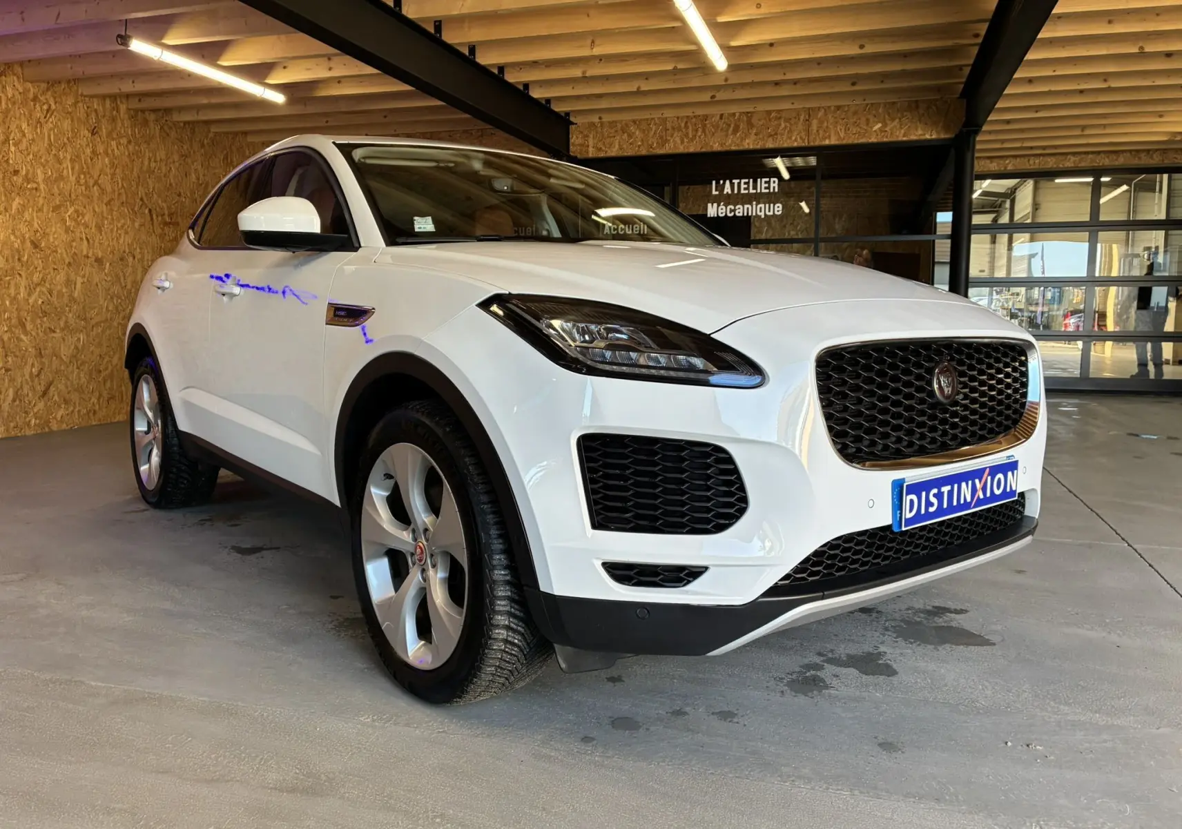 Jaguar E-PACE blanc en 3/4 avant droit, mettant en valeur sa calandre noire et ses jantes argentées dans un garage.