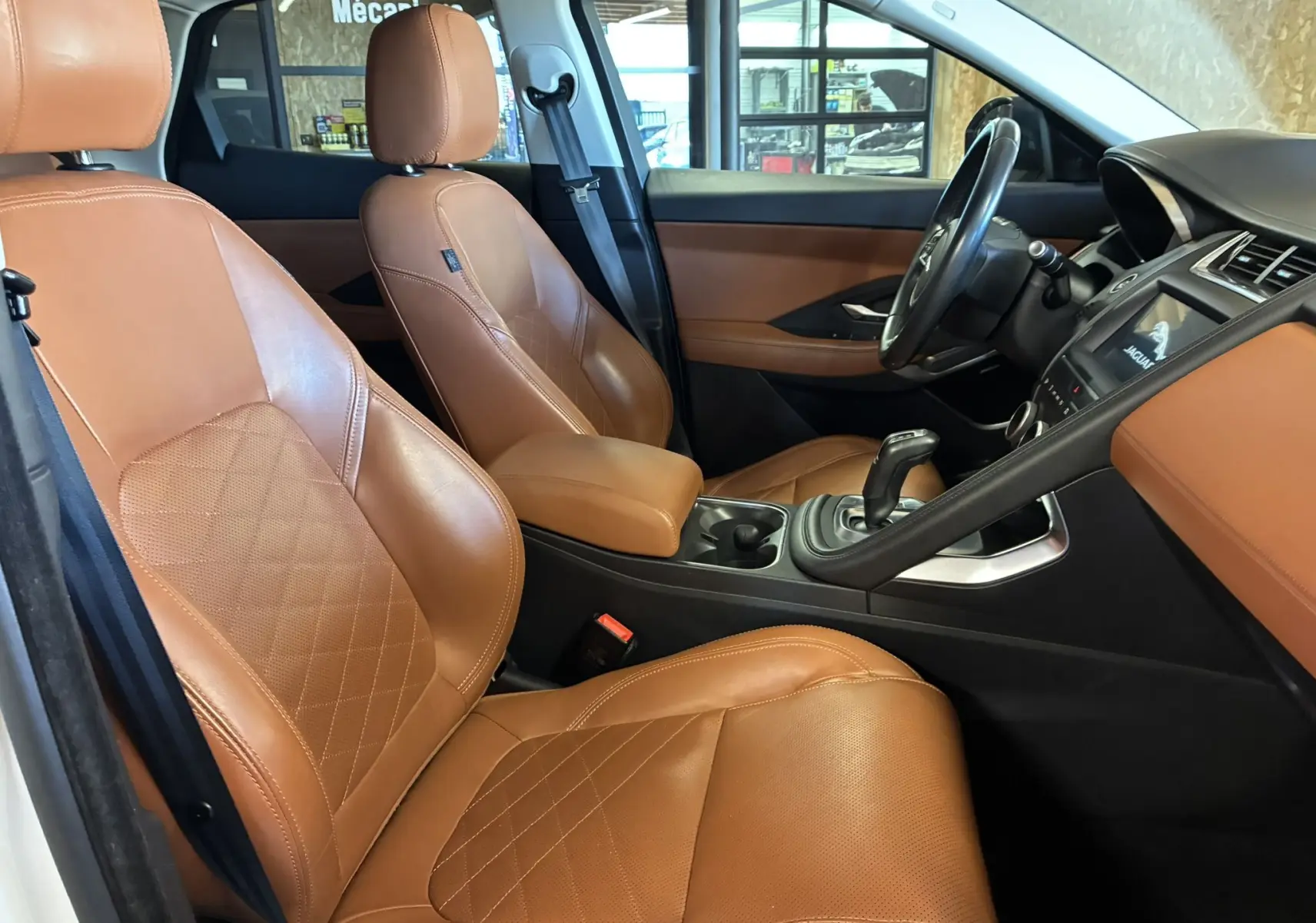 Vue intérieure côté gauche du Jaguar E-PACE 2019, sièges en cuir brun et tableau de bord avec écran tactile allumé.