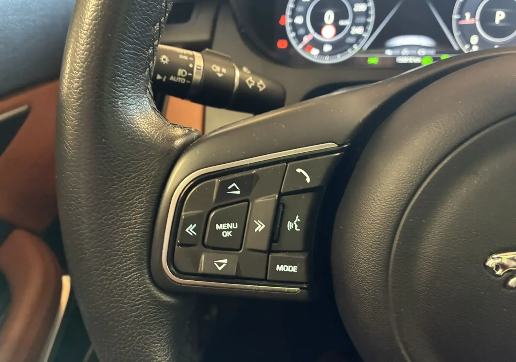 Gros plan sur les commandes gauche du volant noir d’un Jaguar E-PACE 2019, avec tableau de bord numérique en arrière-plan.