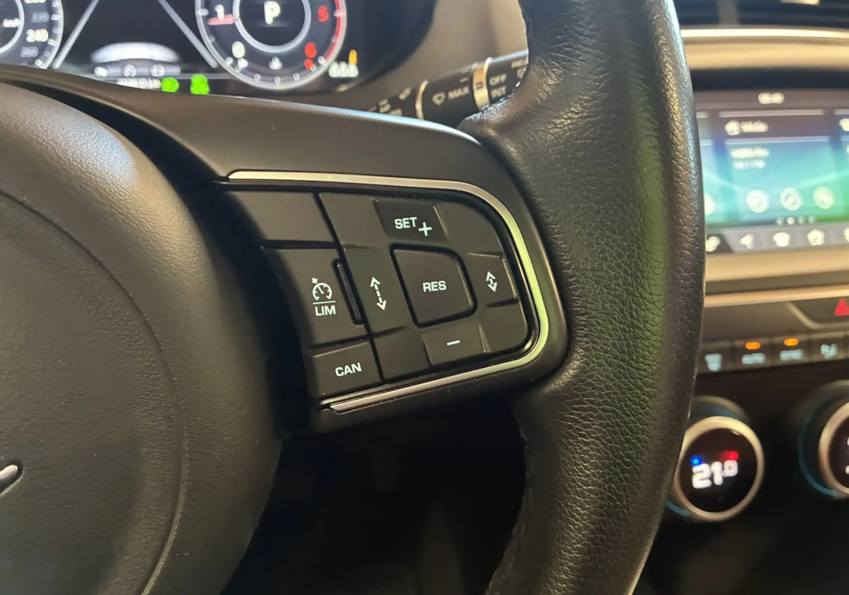 Gros plan sur les commandes au volant en cuir noir du Jaguar E-PACE blanc, avec tableau de bord et écran tactile en arrière-plan.